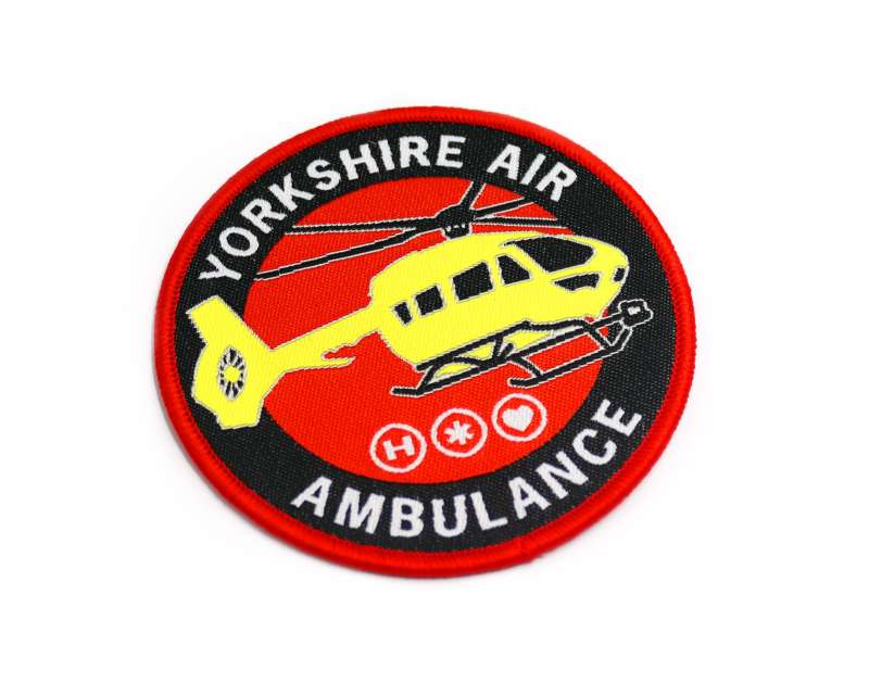A woven patch featuring the yellow helicopter of the Yorkshire air ambulance on a red and black background. The words Yorkshire Air Ambulance encircle the patch.